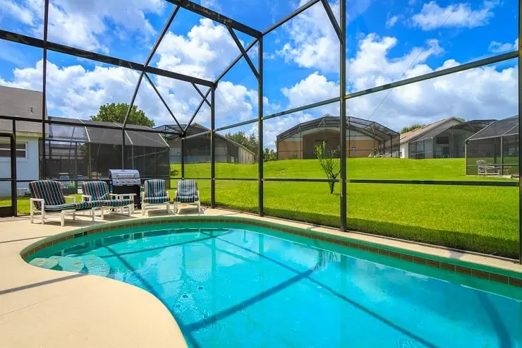 A screened-in backyard pool in a Florida home with lounge chairs and a barbecue grill.