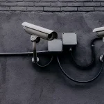 A pair of CCTV surveillance cameras mounted on a wall, representing security and monitoring.