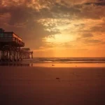 A breathtaking sunset at Cocoa Beach, Florida, with golden skies reflecting on the shoreline and a scenic pier extending over the ocean.