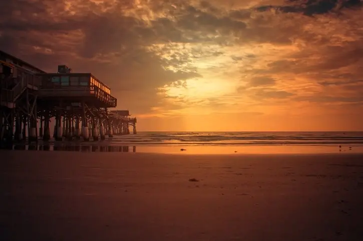 A breathtaking sunset at Cocoa Beach, Florida, with golden skies reflecting on the shoreline and a scenic pier extending over the ocean.