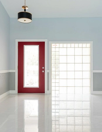 A bright interior of a Florida home with glossy tile flooring, a red door, and a glass block wall.