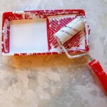 A paint roller and tray with white paint, symbolizing ongoing home maintenance and upkeep costs.
