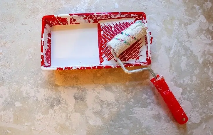 A paint roller and tray with white paint, symbolizing ongoing home maintenance and upkeep costs.