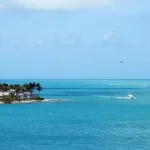 A scenic ocean view of Key West, Florida, featuring waterfront homes, palm trees, and boats on the turquoise waters.