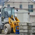 A construction vehicle at a home construction site with scaffolding and concrete blocks.