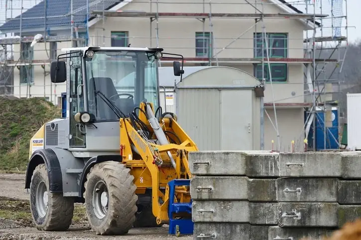 A construction vehicle at a home construction site with scaffolding and concrete blocks.