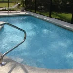 A screened-in backyard pool with metal handrails and lounge chair, surrounded by a patio and greenery in Florida.