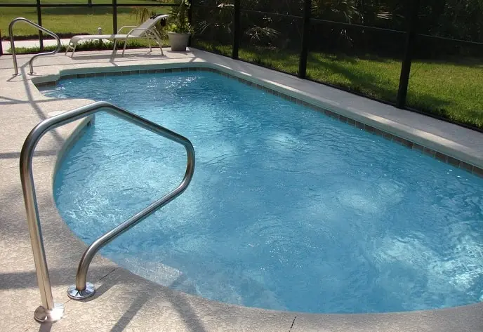 A screened-in backyard pool with metal handrails and lounge chair, surrounded by a patio and greenery in Florida.