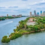 A scenic view of Tampa Bay with waterfront homes, lush greenery, and the downtown skyline in the background.