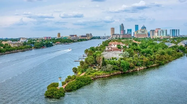 A scenic view of Tampa Bay with waterfront homes, lush greenery, and the downtown skyline in the background.